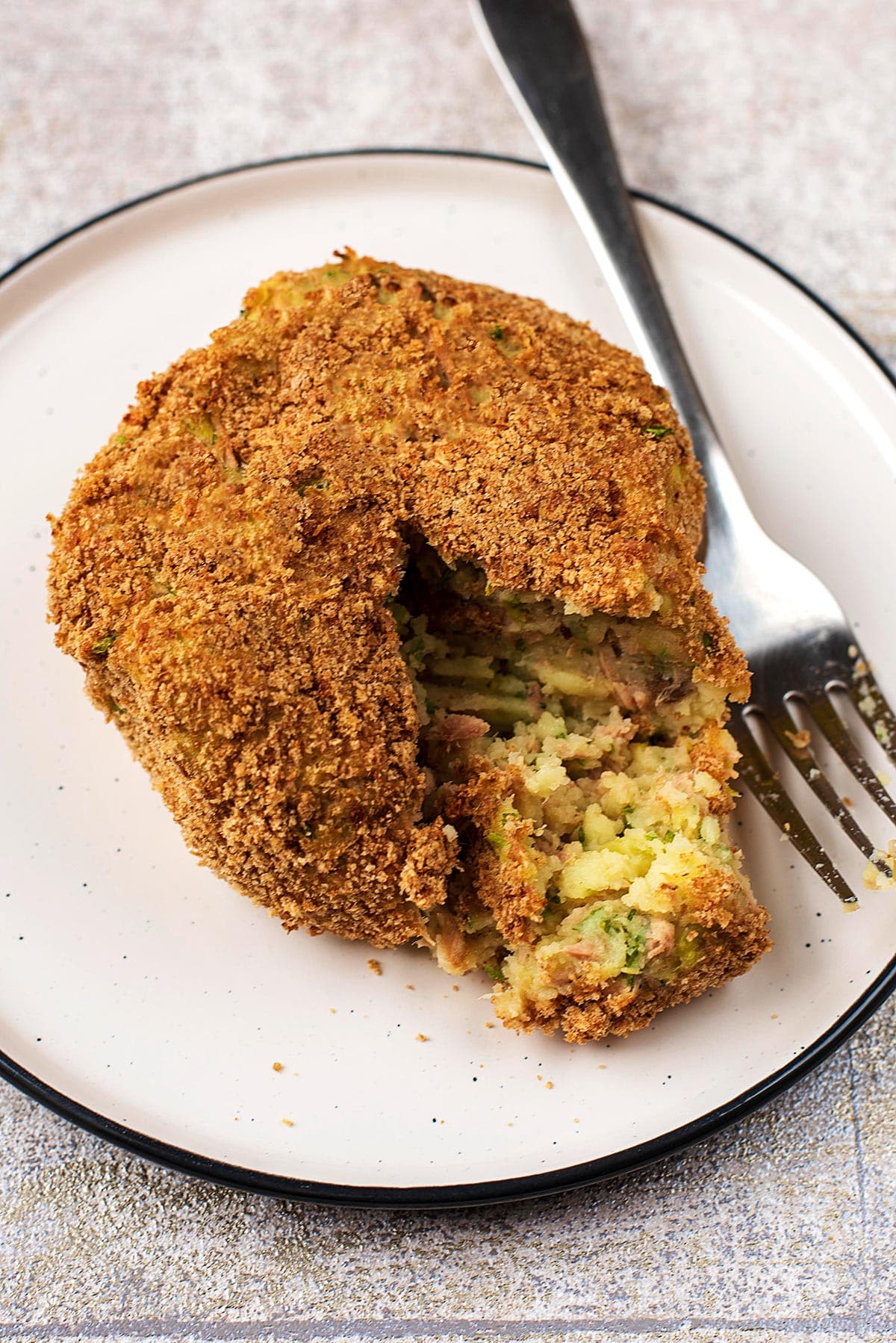 Tuna fish cake on a plate, cut open with a fork.