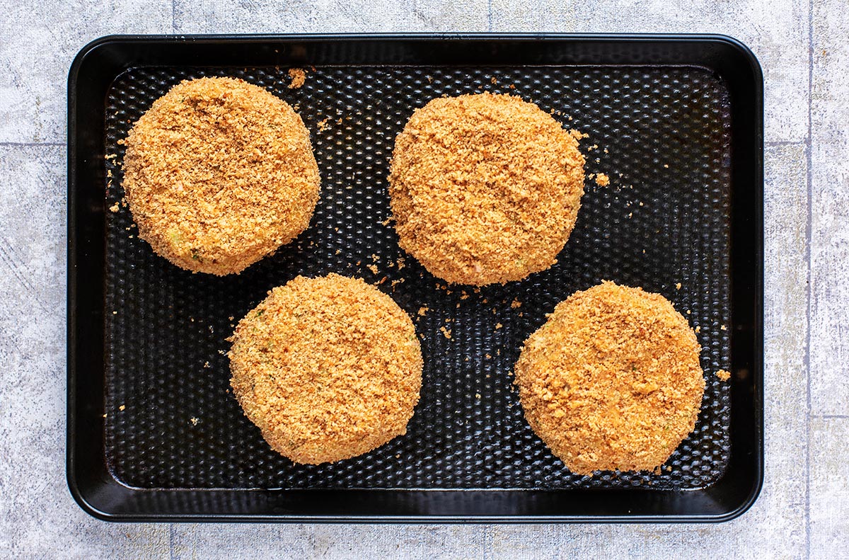 A black baking tray with four breaded fishcakes on it.