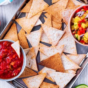 A metal tray covered in baked tortilla chips with two bowls of dip.