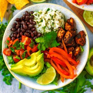 A chicken burrito bowl next to half an avocado and some coriander.