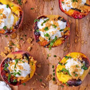 A wooden board with grilled peaches, honey and a spoonful of ice cream.