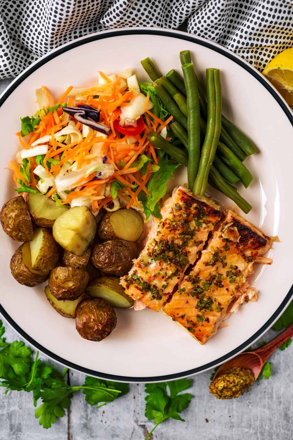 Two cooked salmon fillets on a plate with roasted potatoes, green beans and salad.