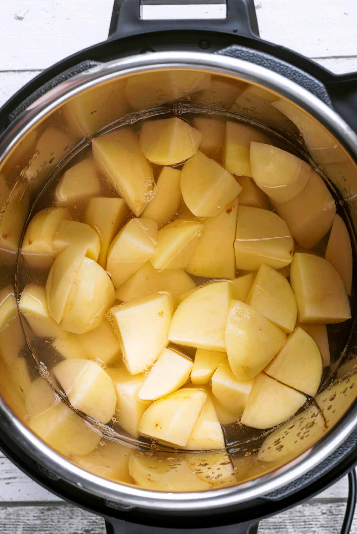 An instant pot containing peeled and chopped potatoes.