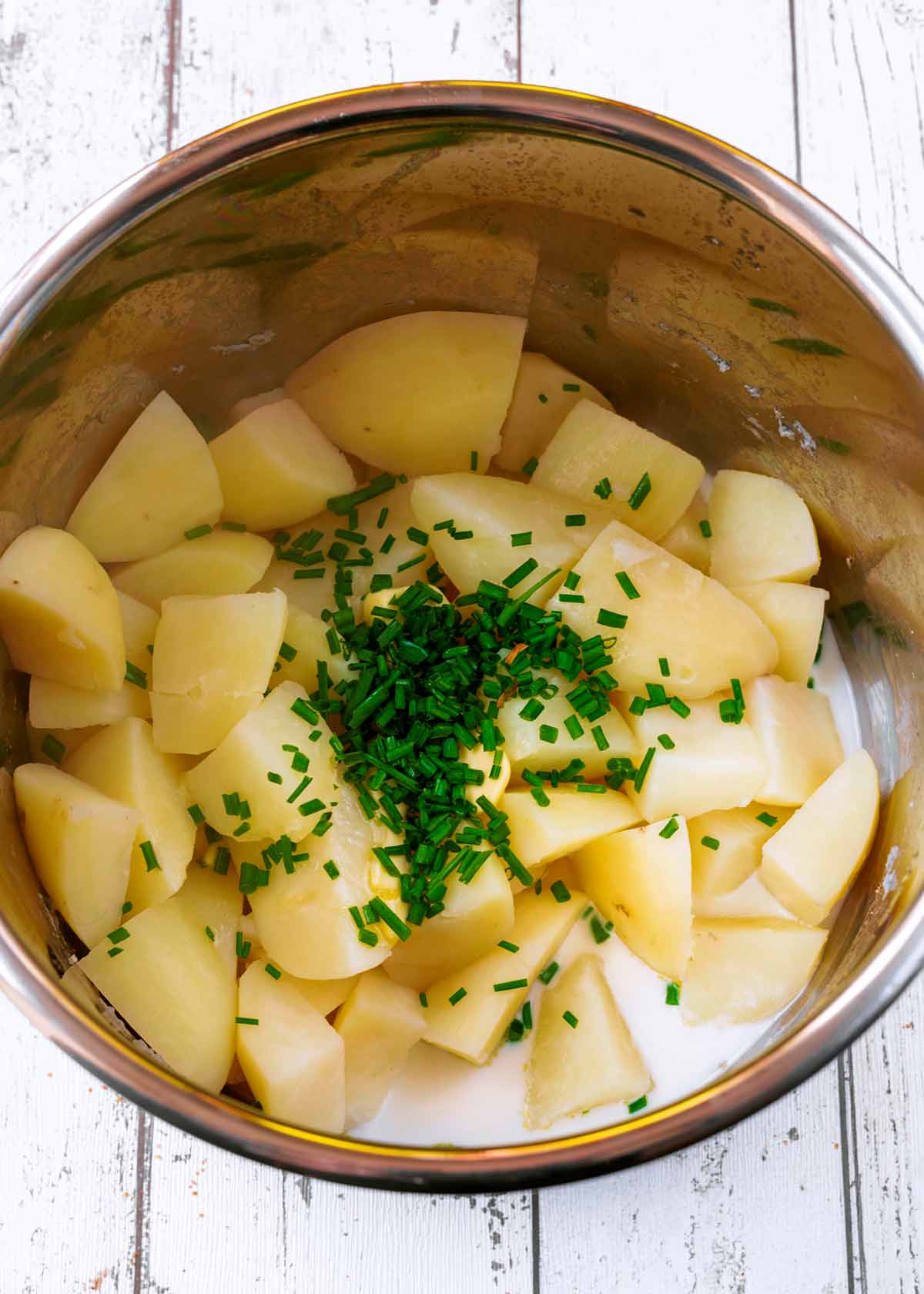 An instant pot containing cooked shopped potatoes, milk, butter and chopped chives.