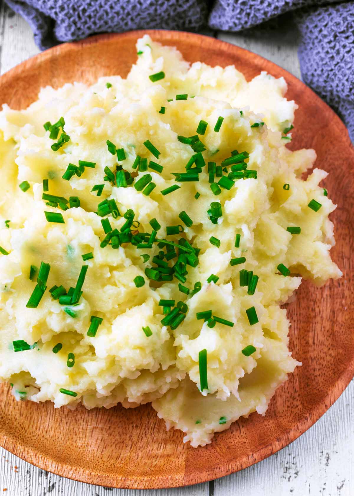 A wooden plate with a large serving of Mashed Potatoes.