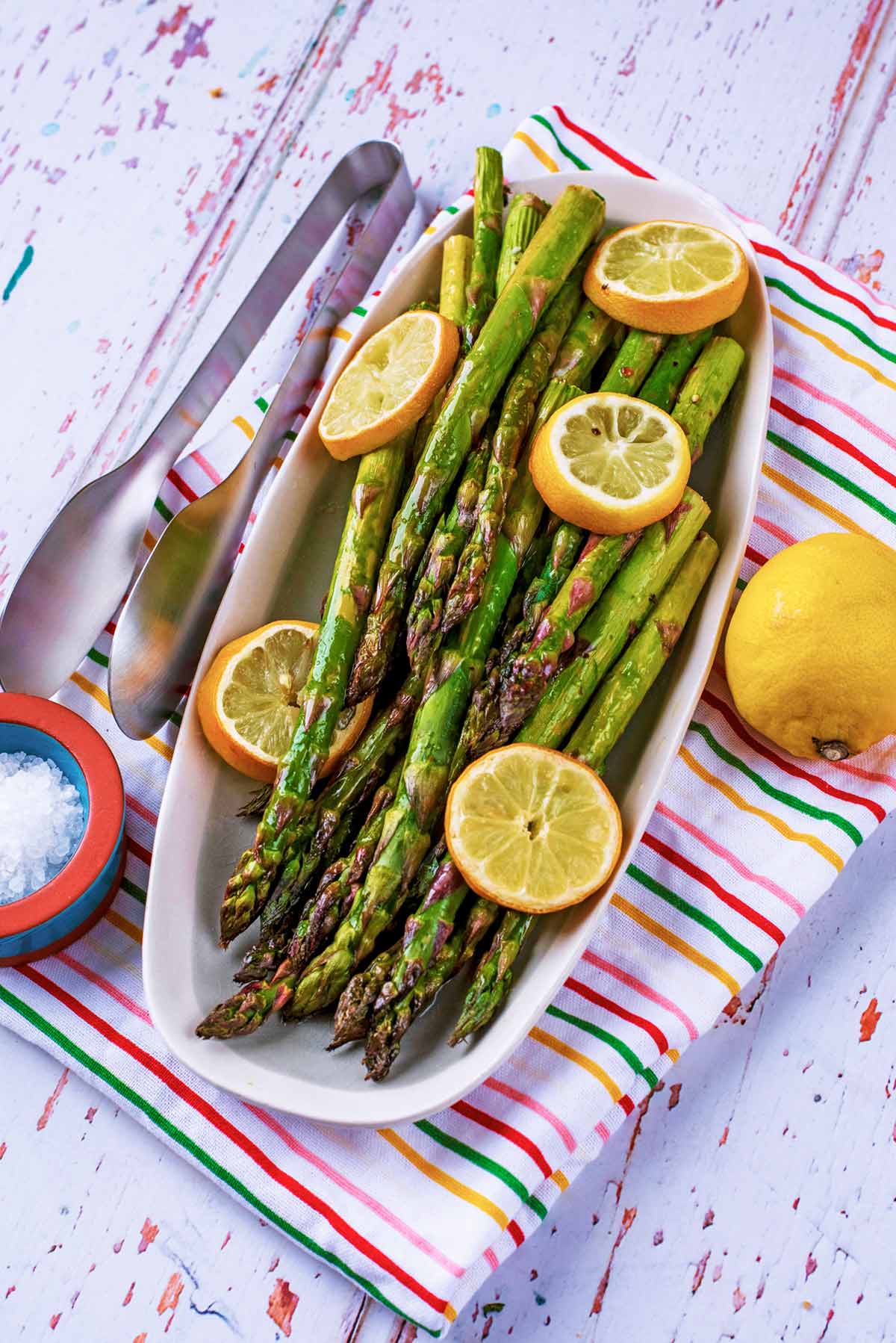 A plate of cooked asparagus and lemon slices on a plate sat on a striped towel.