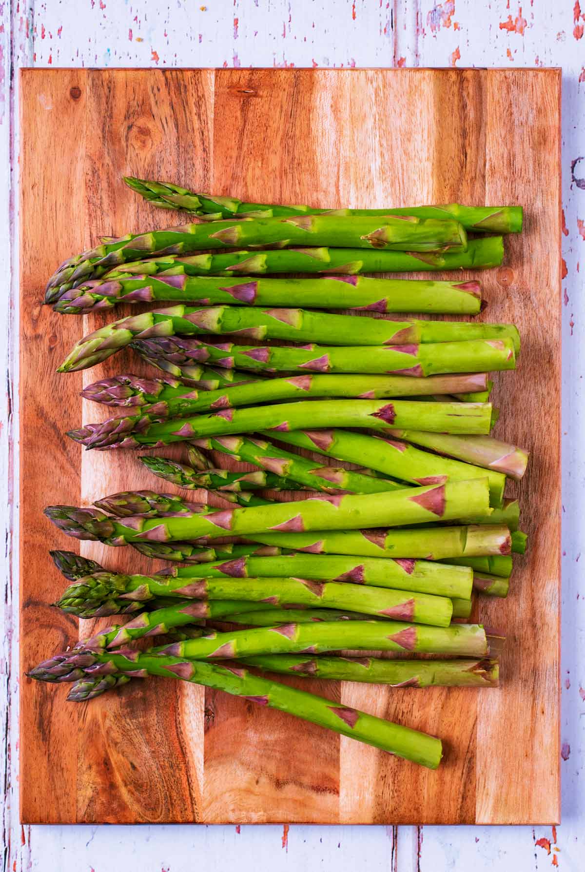 A wooden chopping board with raw asparagus spears on it.