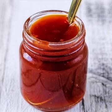 A small jar of sweet and sour sauce with a spoon sticking out of it