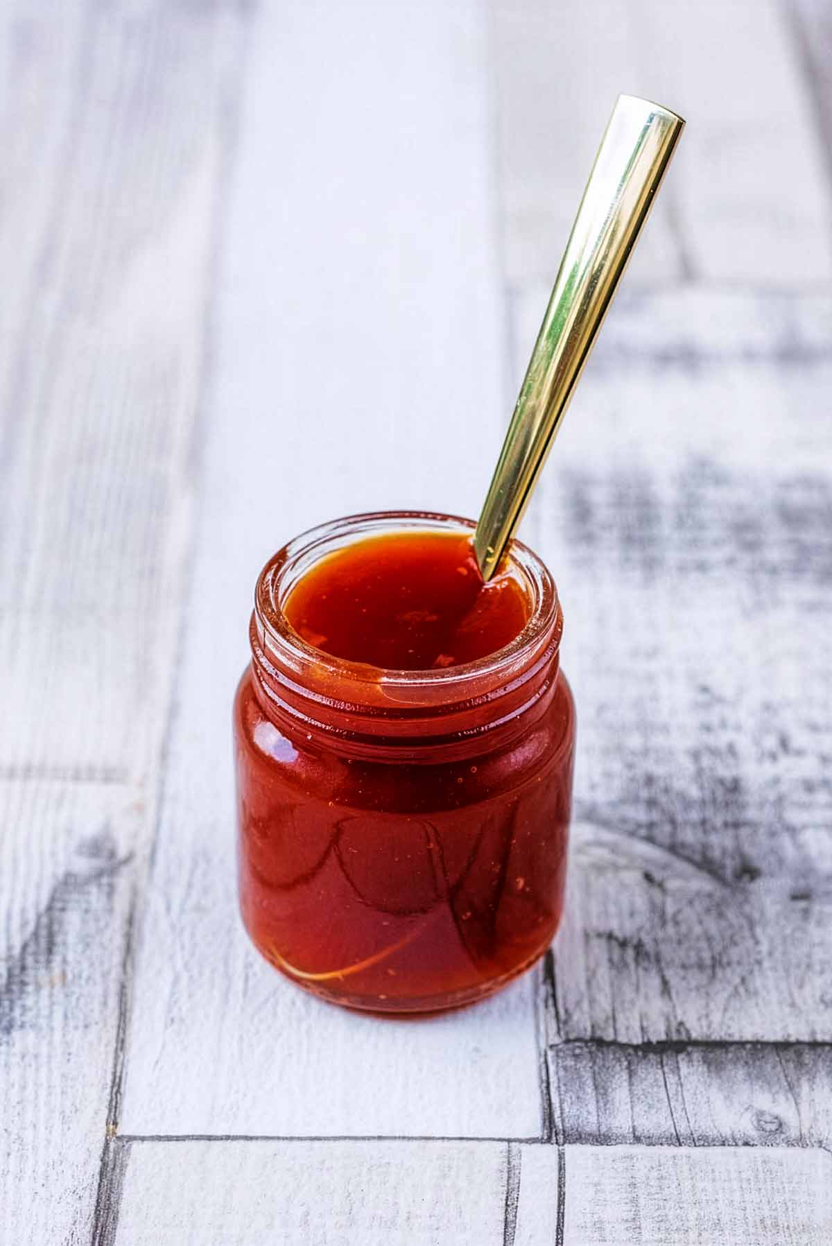 A small jar of sweet and sour sauce with a spoon sticking out of it