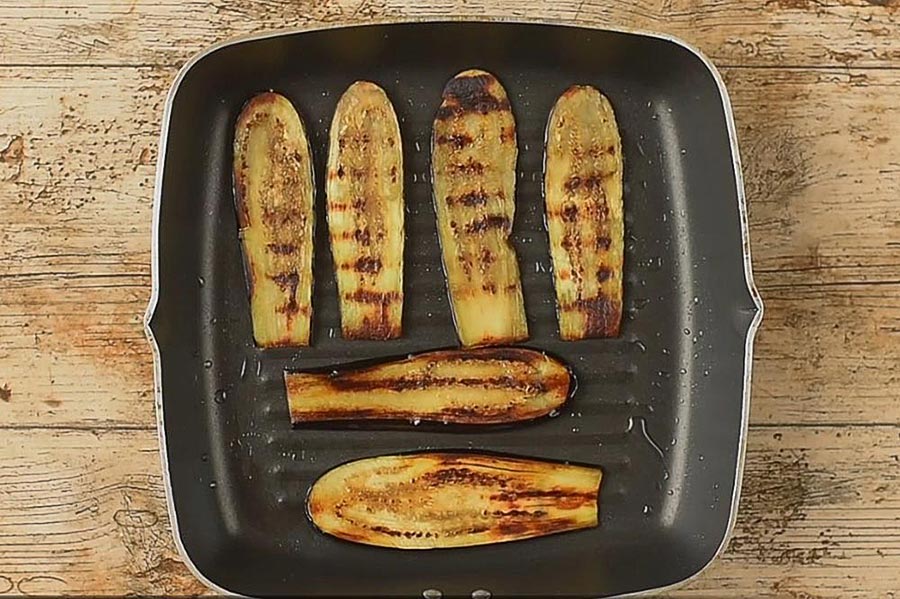 Sliced aubergines cooking in a griddle pan.