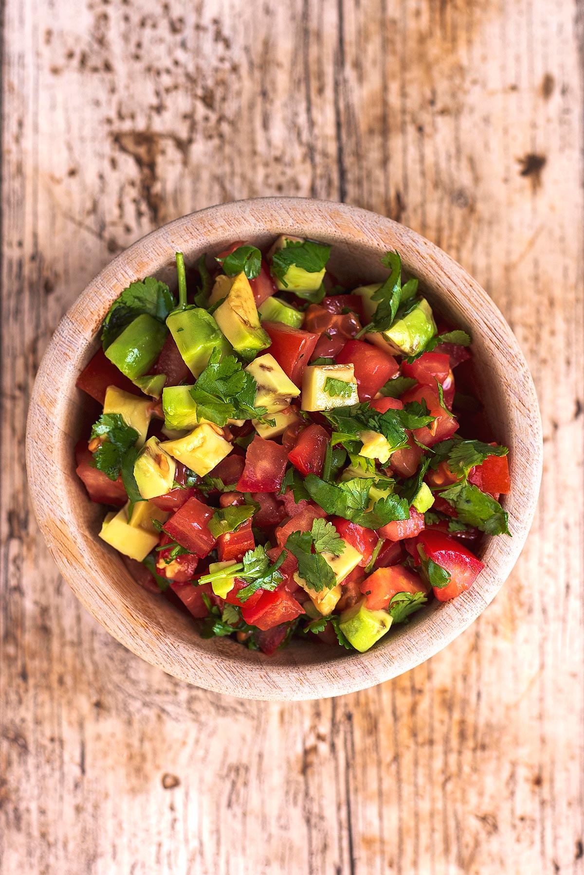 A small wooden bowl containing chopped tomato and avocado salsa.
