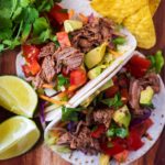 Two Slow Cooker Beef Tacos on a wooden board with two lime wedges