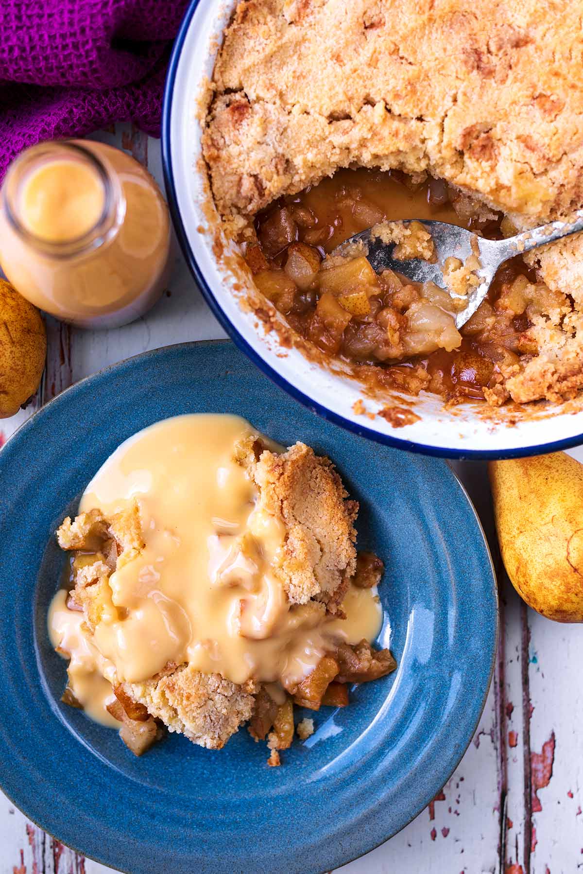 A bowl of apple and pear crumble topped with custard.