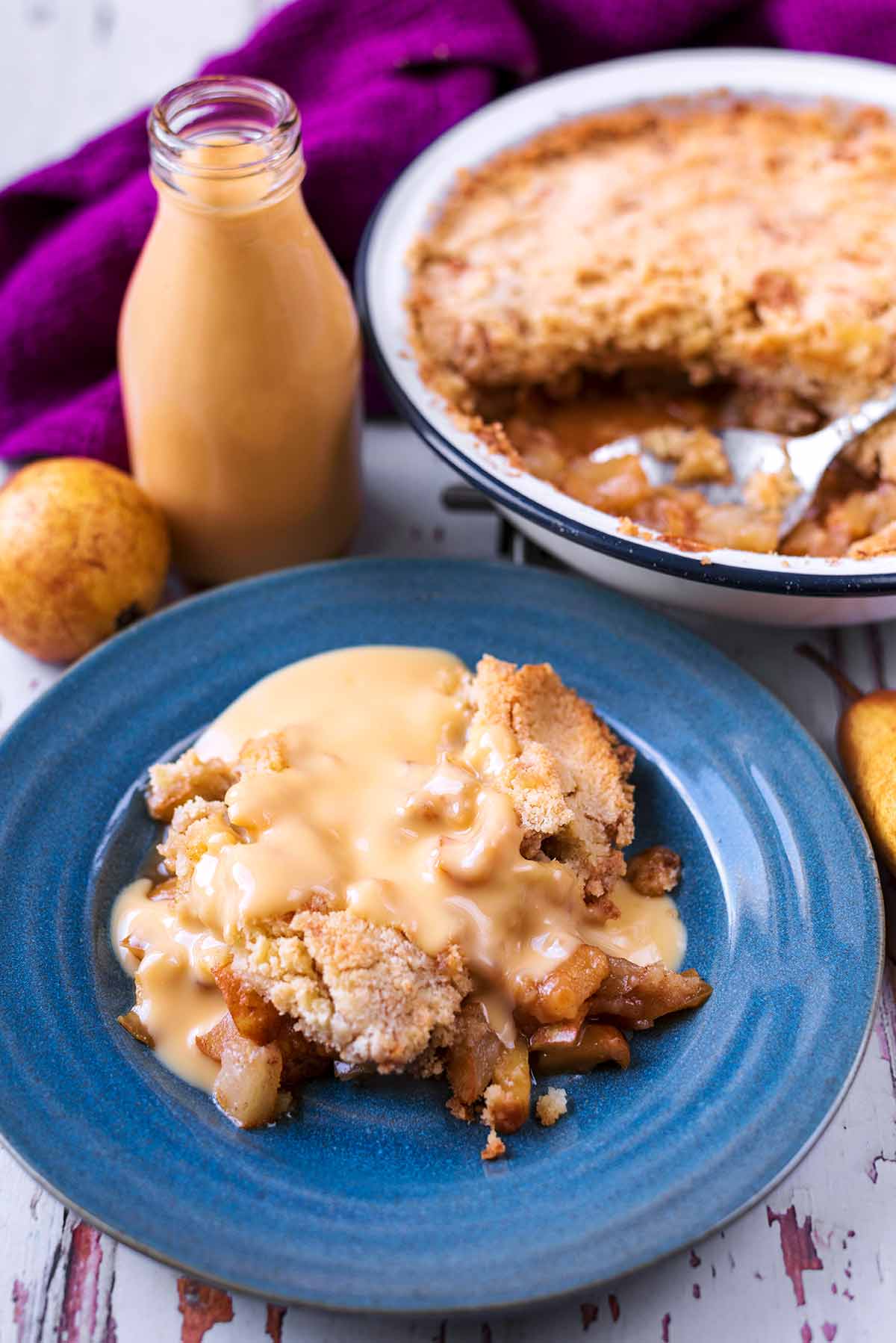 A bowl of custard covered crumble in front of a dish of more crumble.