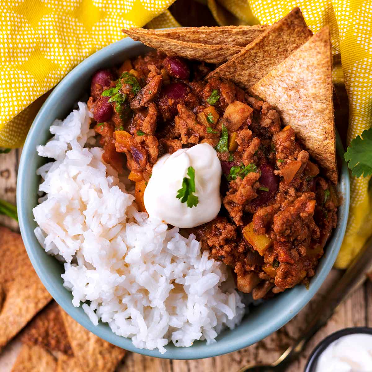 A bowl of chilli con carne and rice with a dollop of sour cream on top.