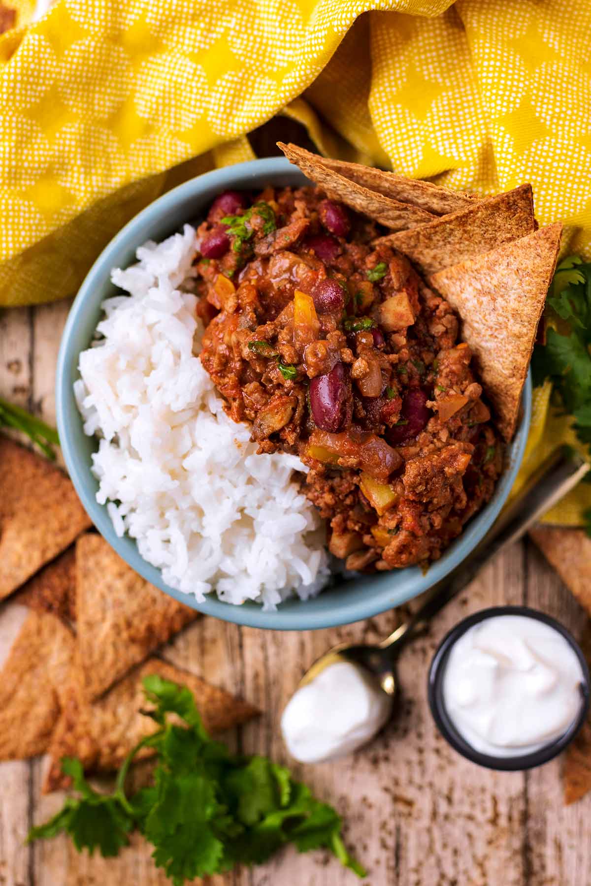 A bowl of chilli con carne and rice with tortilla chips sticking out of the chilli.