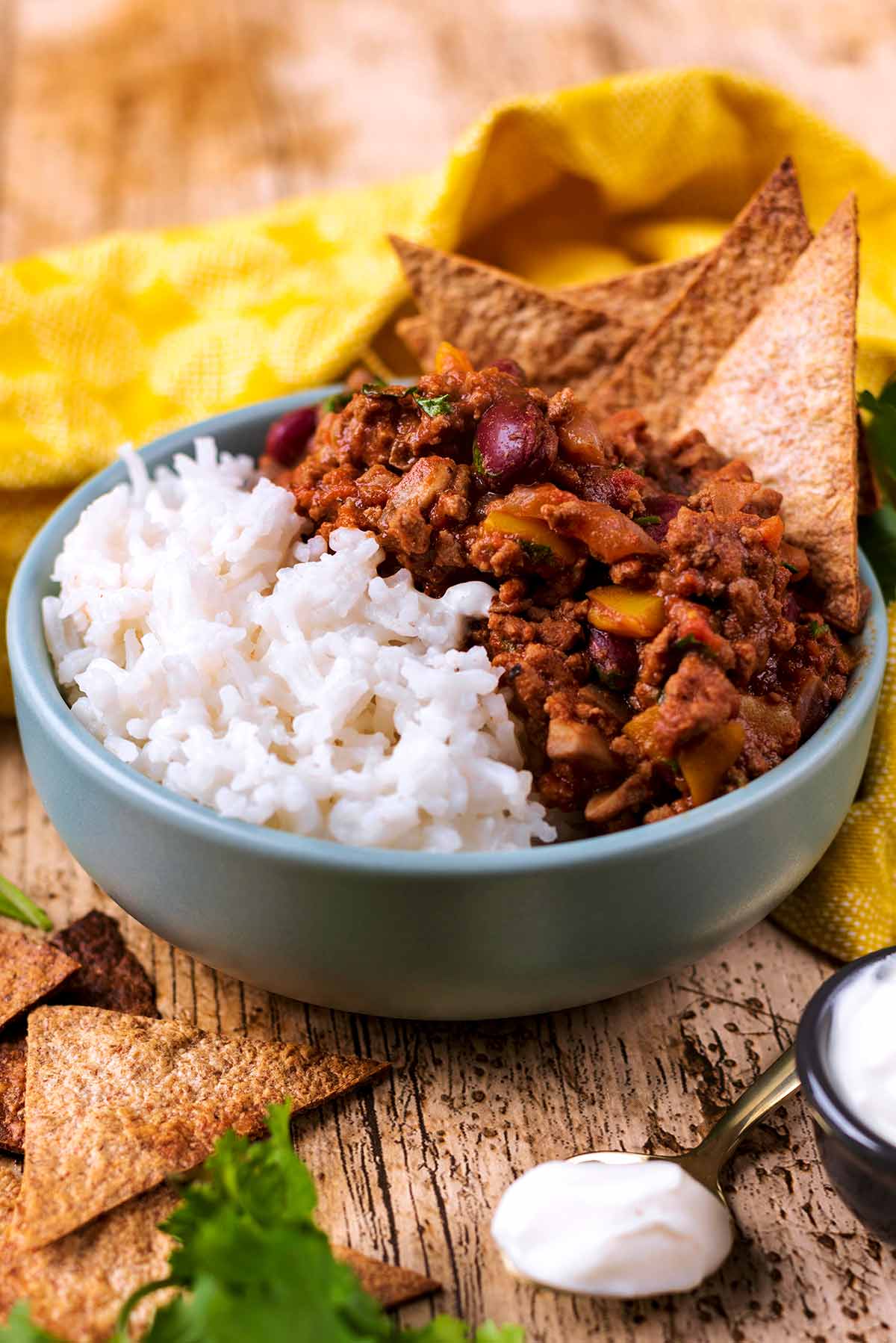 Chilli and rice in a blue bowl with tortilla chips.