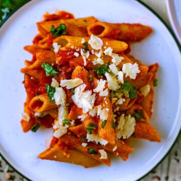 A plate of penne arrabiata topped with chopped herbs and Parmesan shavings.