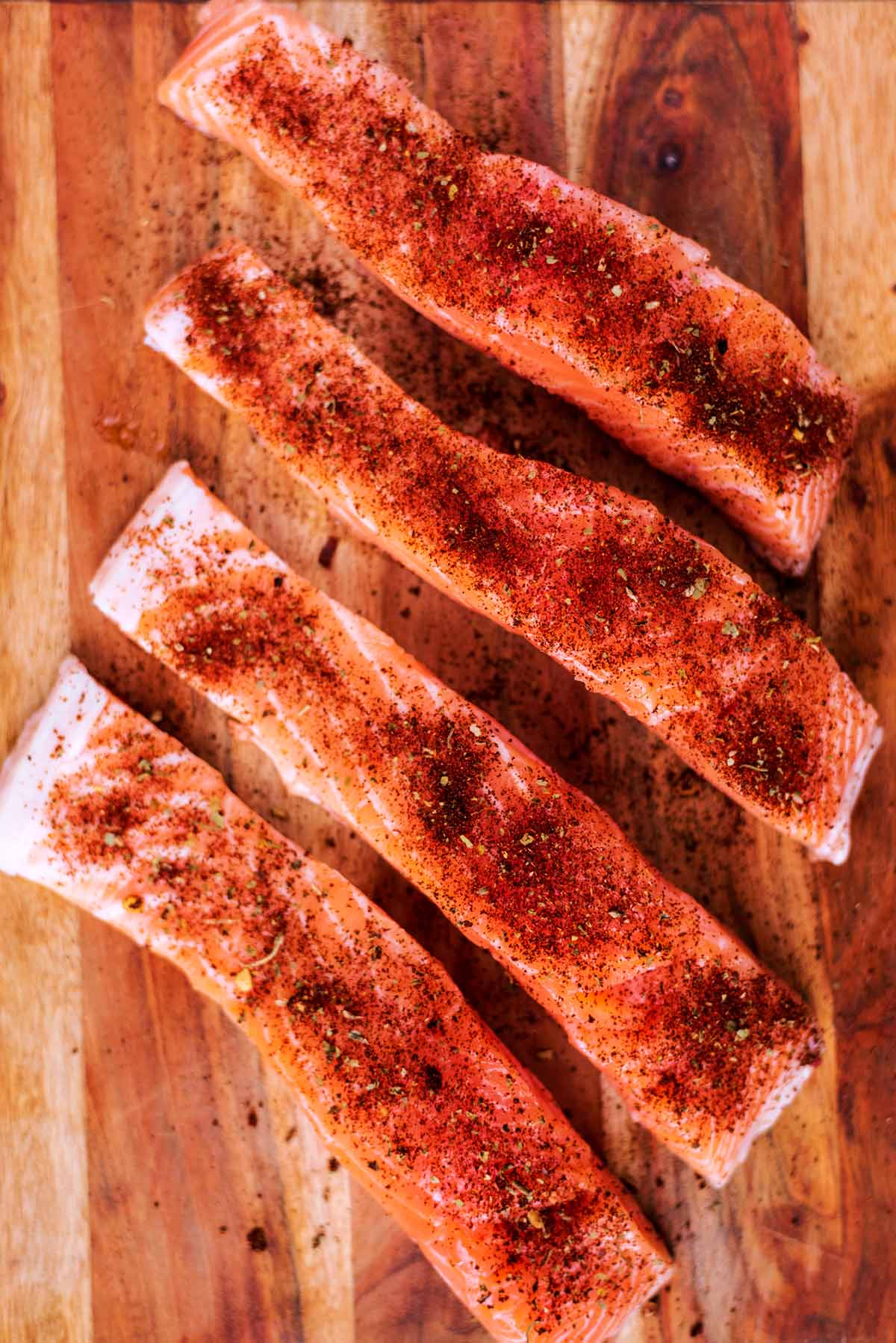 Four salmon fillets on a wooden board coated in taco seasoning.