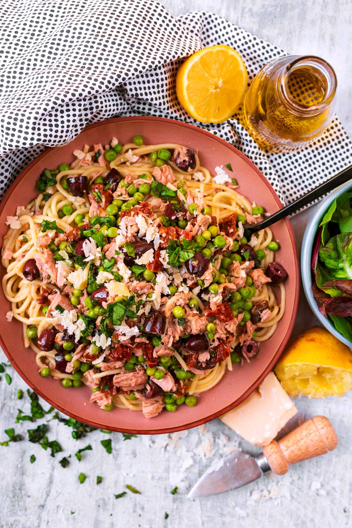 A plate of spaghetti mixed with tuna and vegetables next to a bowl of salad