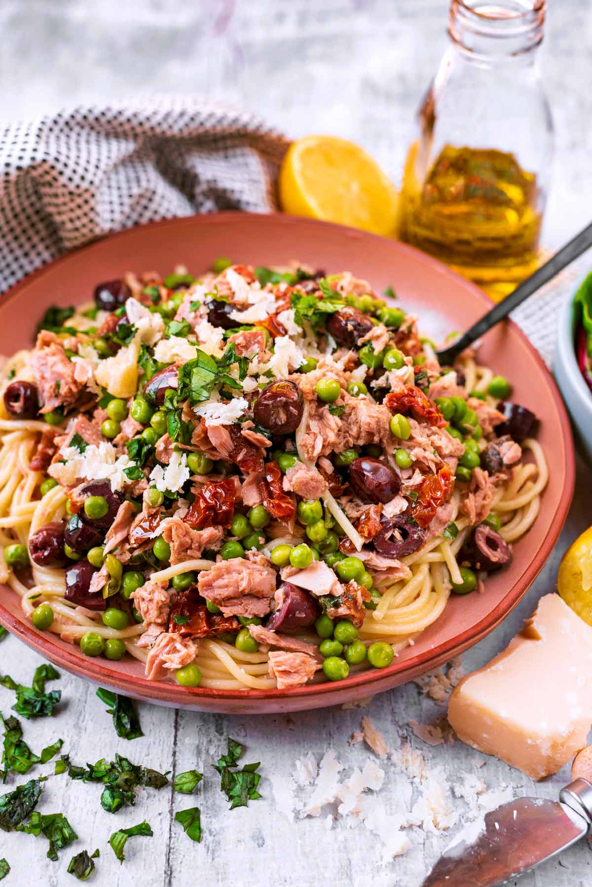 A plate of tuna and vegetable spaghetti next to a small block of Parmesan.