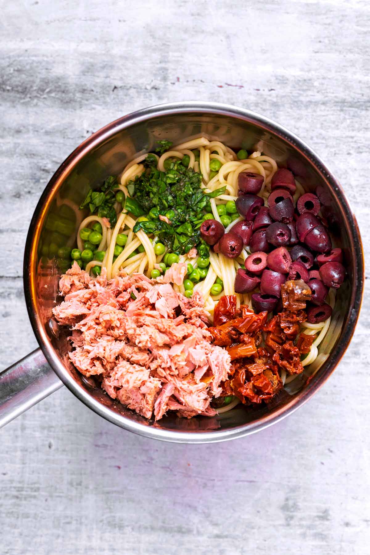 Cooked spaghetti in a pan with tuna, olives, tomatoes, peas and herbs.