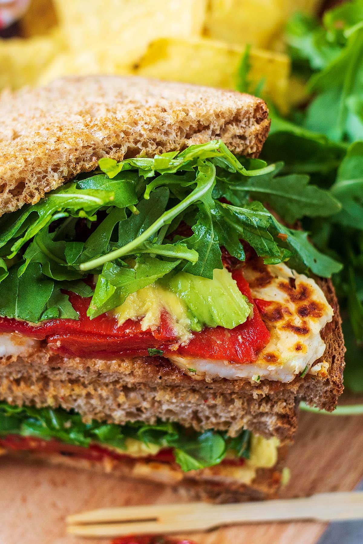 Halloumi, red peppers, avocado and lettuce spilling out of a sandwich.