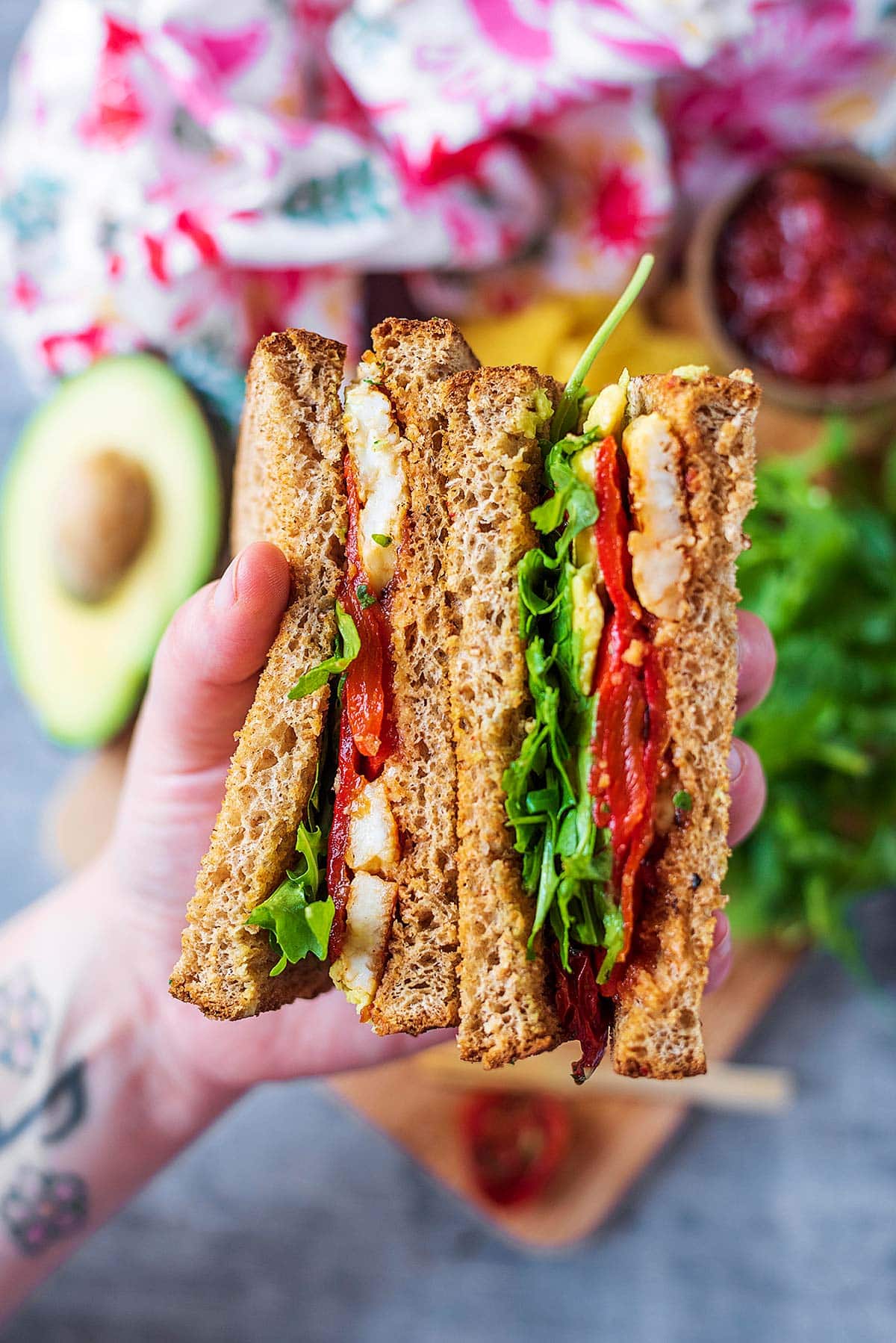 A hand holding two halves of a halloumi and salad sandwich.