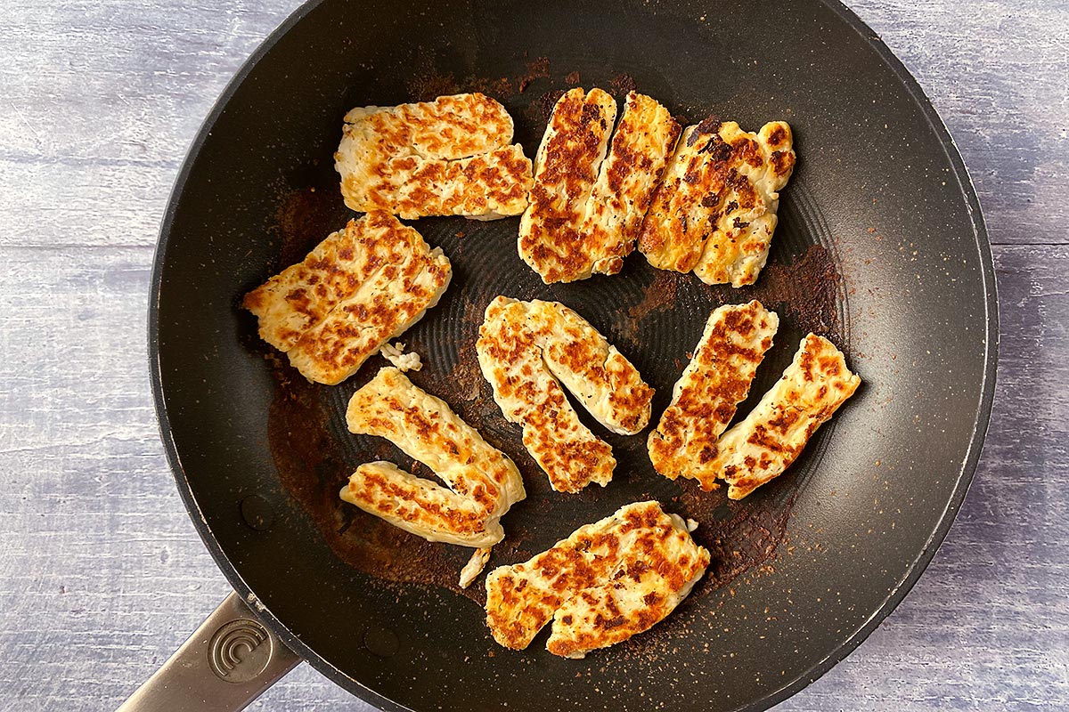 A frying pan with slices of halloumi cooking in it.