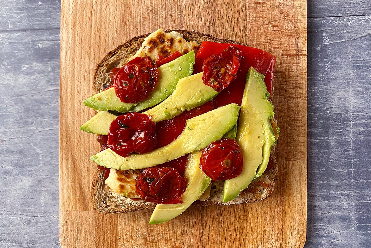 A slice of toasted bread topped with chutney, halloumi, red pepper, avocado and tomatoes.
