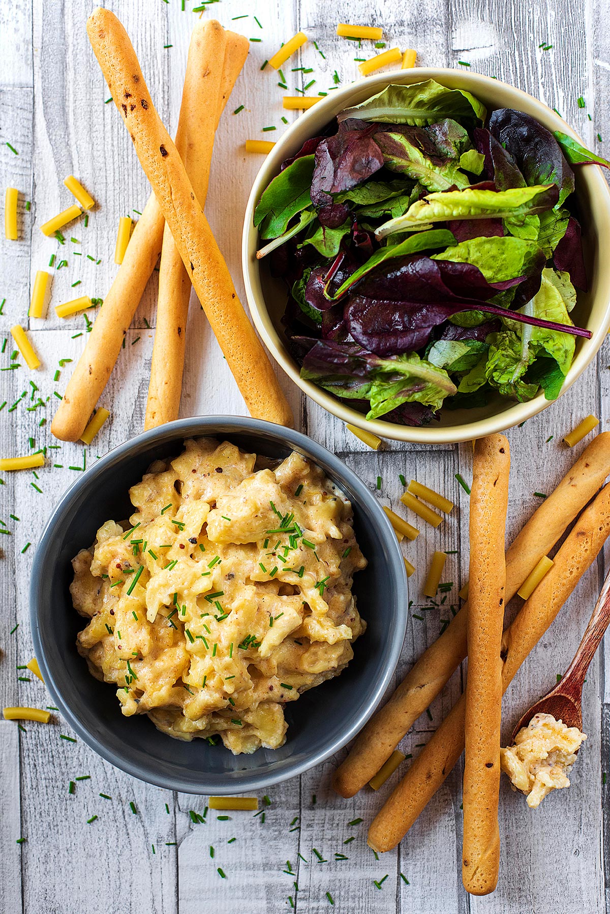 A bowl of mac and cheese next to a bowl of salad leaves and some bread sticks