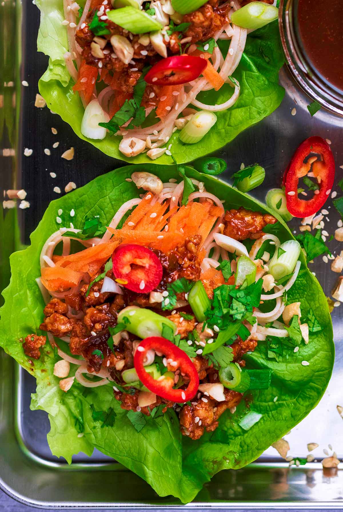 A large lettuce leaf topped with ground chicken, vegetables and sesame seeds.
