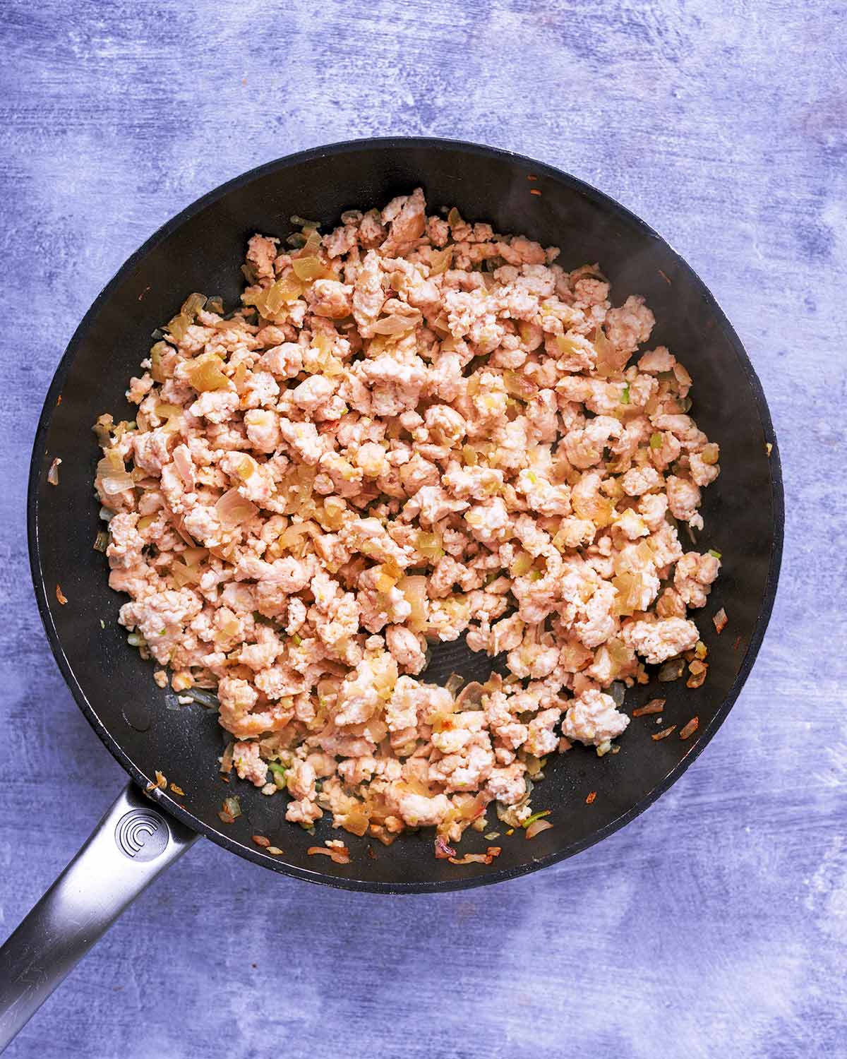 A frying pan with ground chicken cooking in it.