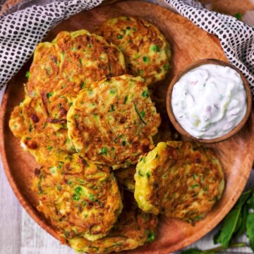 Easy Courgette Fritters on a wooden plate with a bowl of tzatziki.