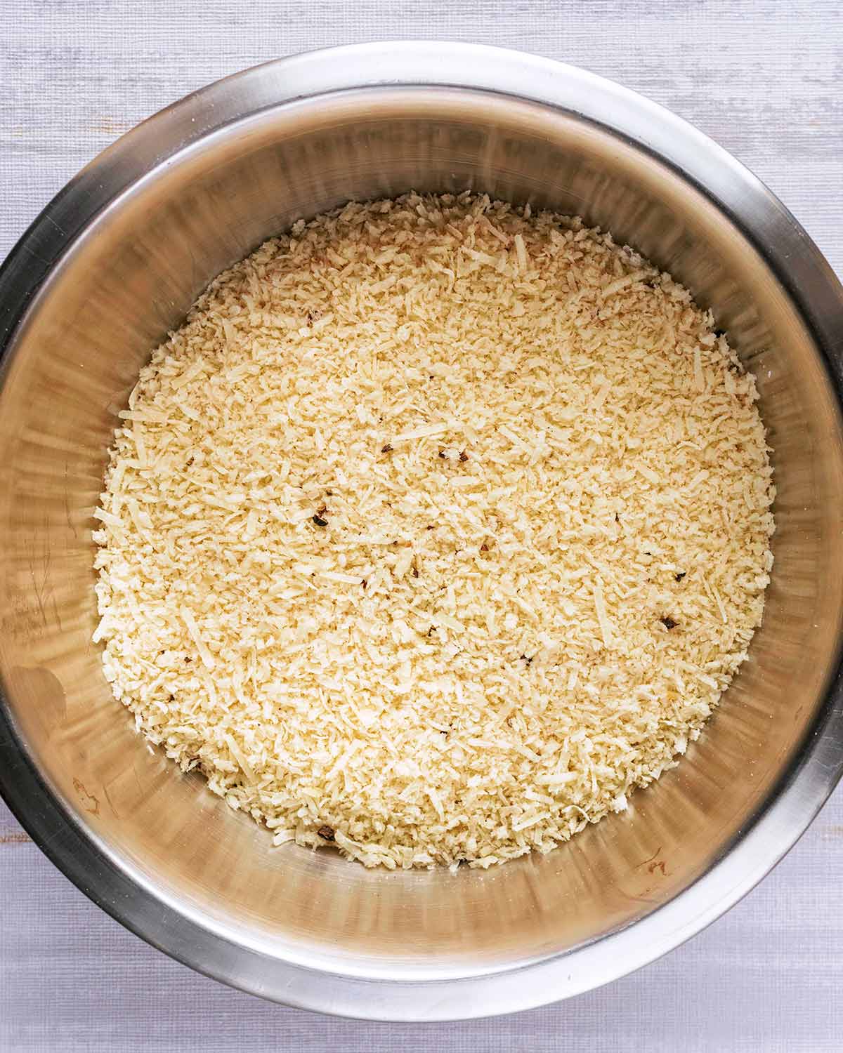A mixing bowl full of breadcrumbs, grated Parmesan and seasoning.