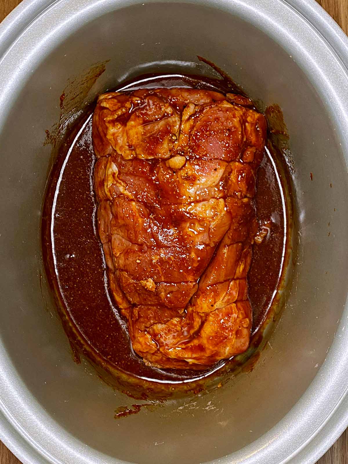 Pork shoulder in a slow cooker with marinade poured over it.