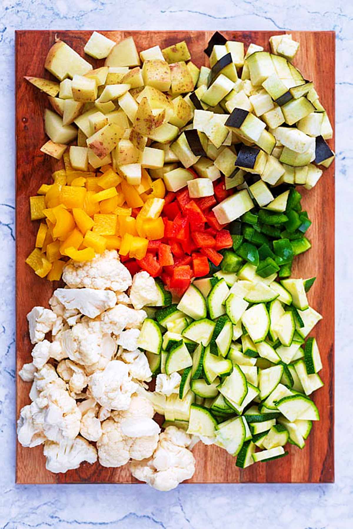 A wooden chopping board covered in chopped vegetables.