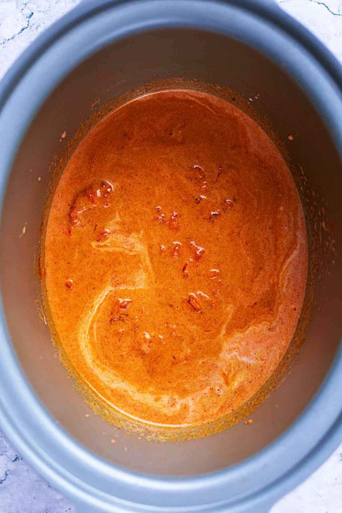 A slow cooker bowl with an uncooked curry sauce in it.