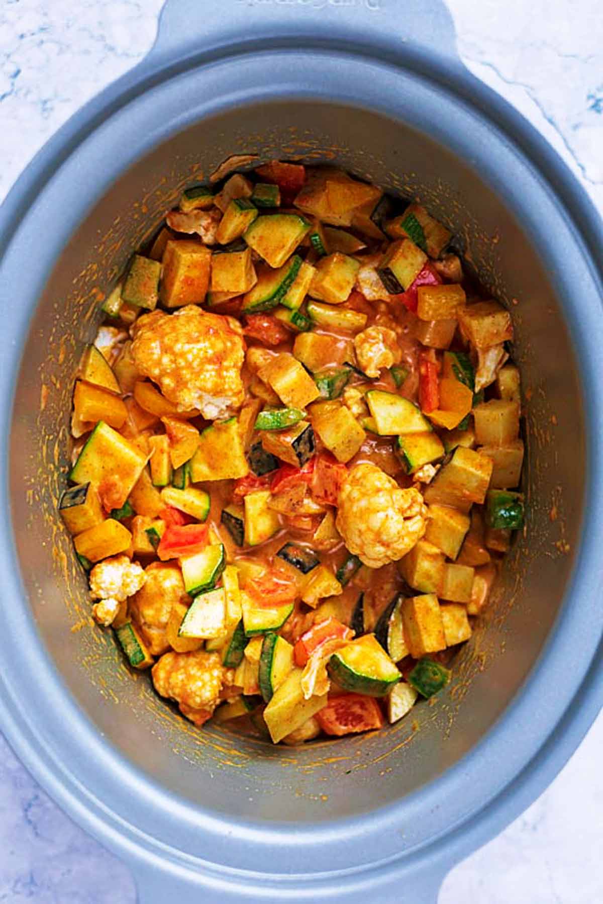 Chopped vegetables in a curry sauce in a slow cooker bowl.