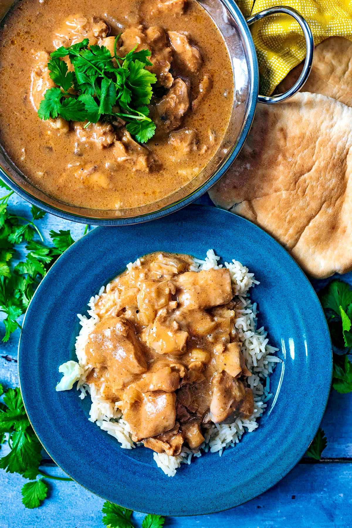 A plate of curry and rice next to a balti dish containing more curry and some naan breads.