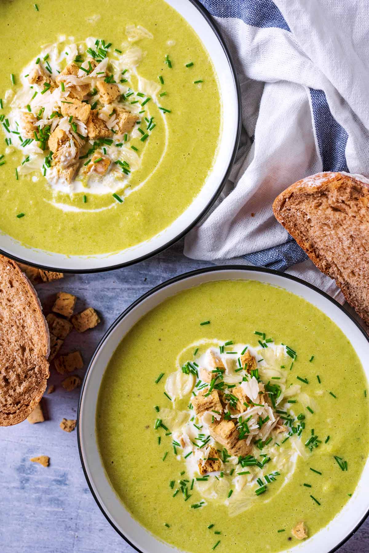 Two bowls of asparagus soup topped with croutons, Parmesan and chives.