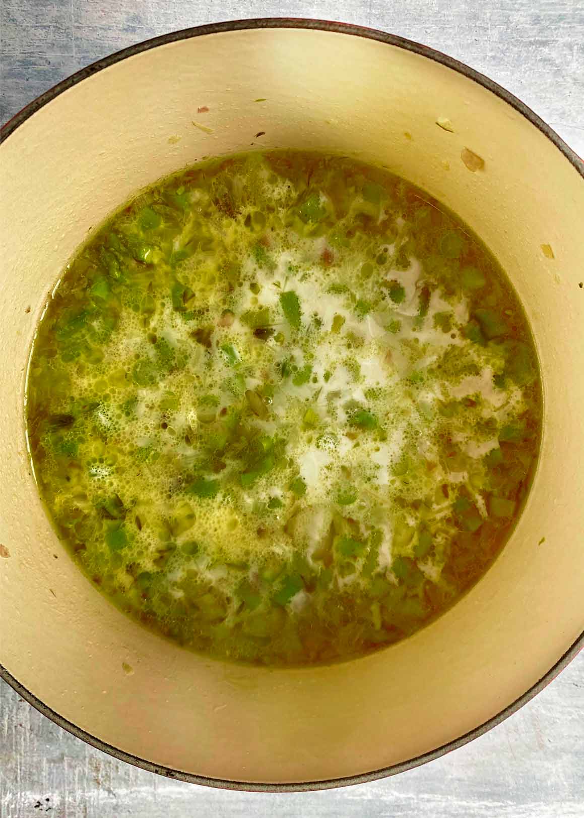 A large cooking pot containing stock, cream, asparagus and shallots.