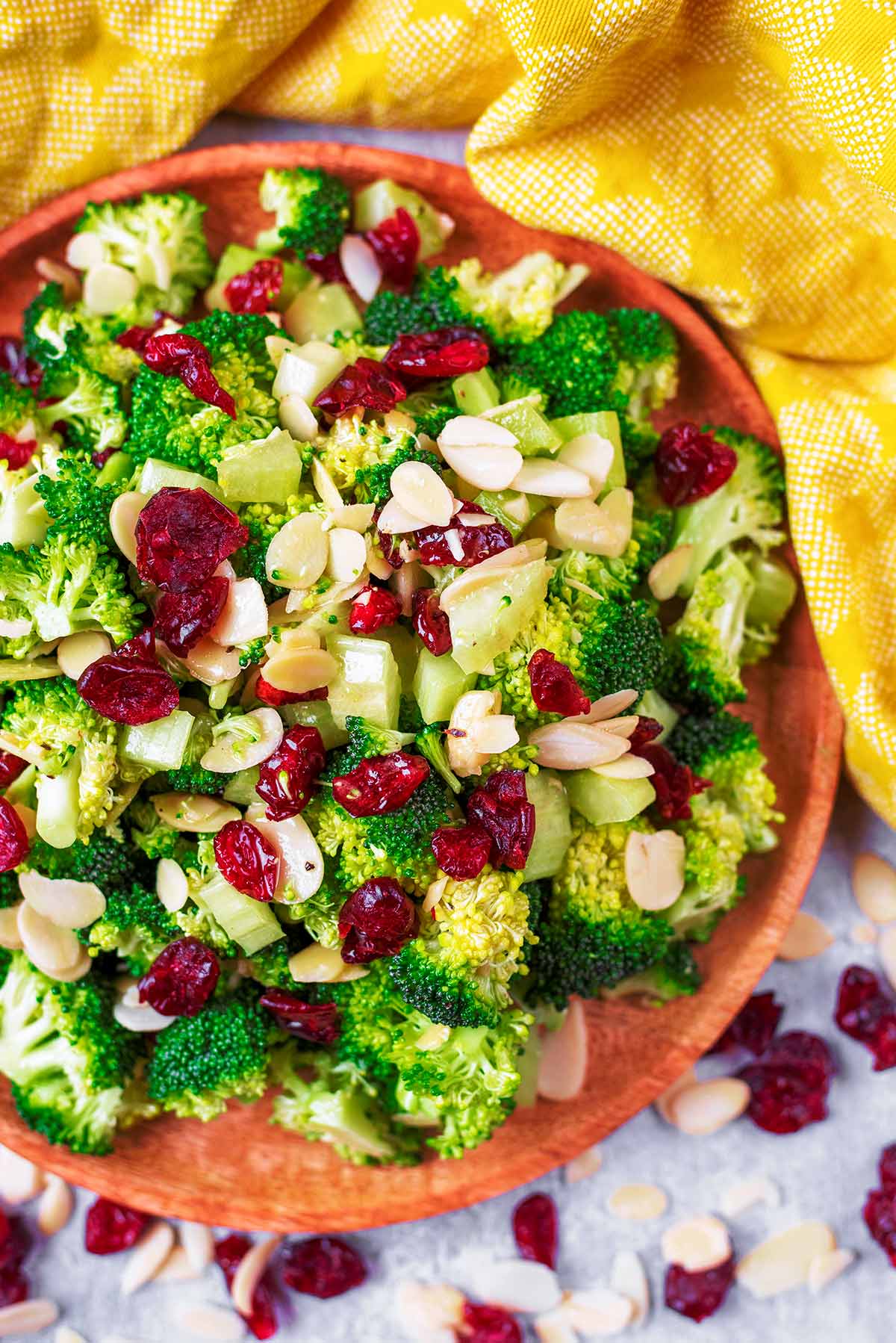A salad of raw broccoli, cranberries and almonds on a wooden plate.