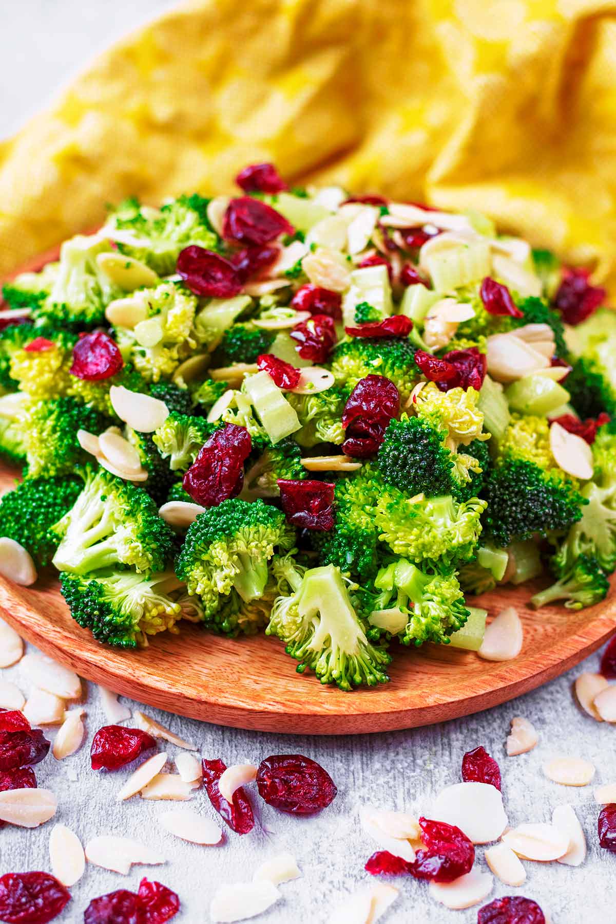 A wooden plate with a big pile of broccoli florets, cranberries and almond flakes.