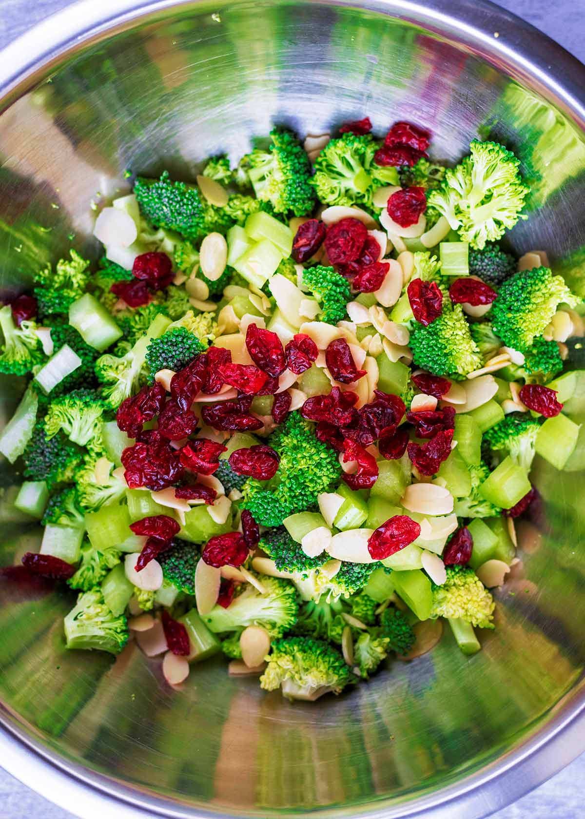 A large mixing bowl containing broccoli florets, cranberries and almonds.