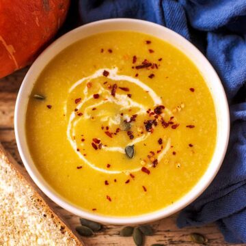 A bowl of pumpkin soup topped with a swirl of cream, pumpkin seeds and chilli flakes.
