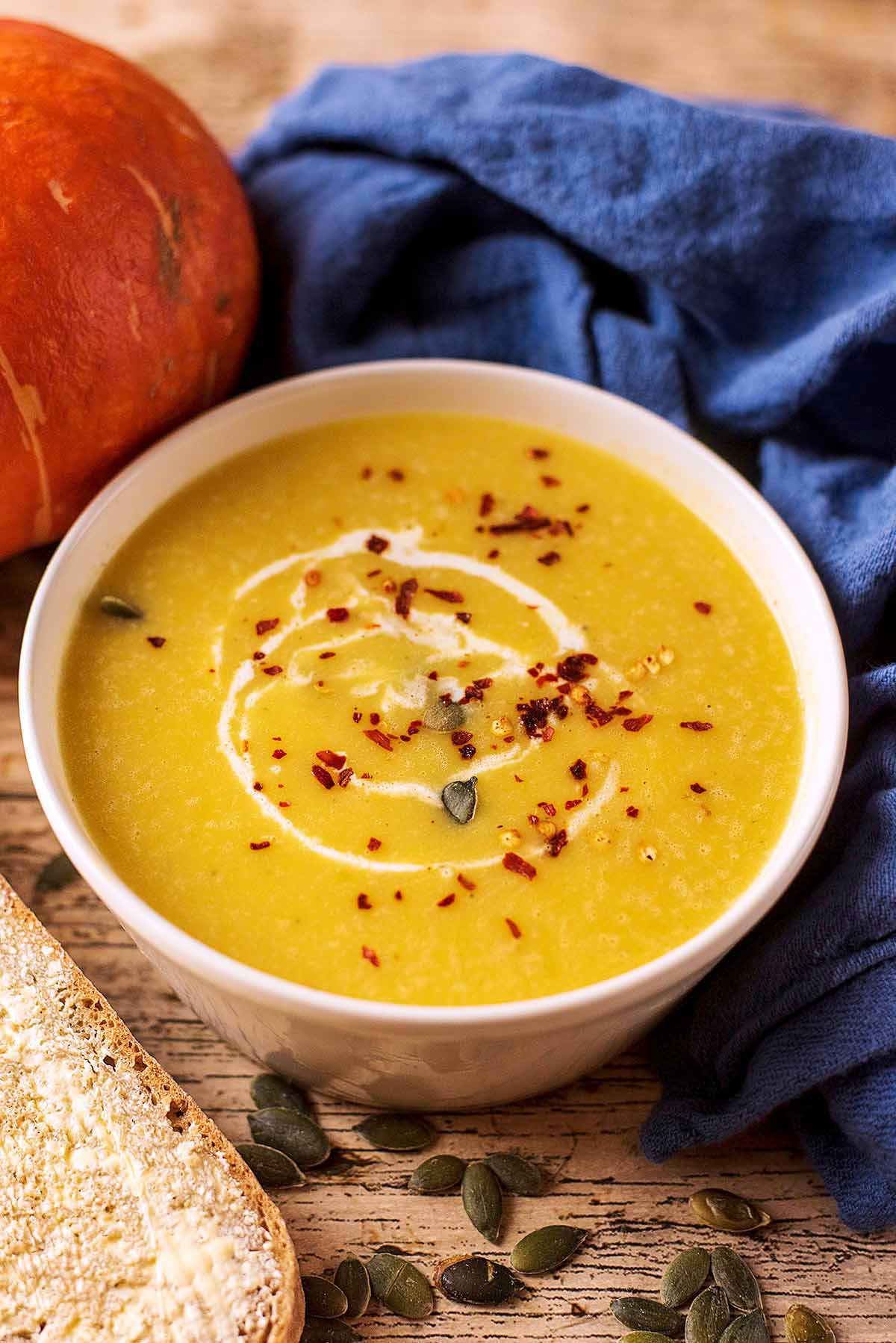 Pumpkin soup in a bowl in front of a blue towel.