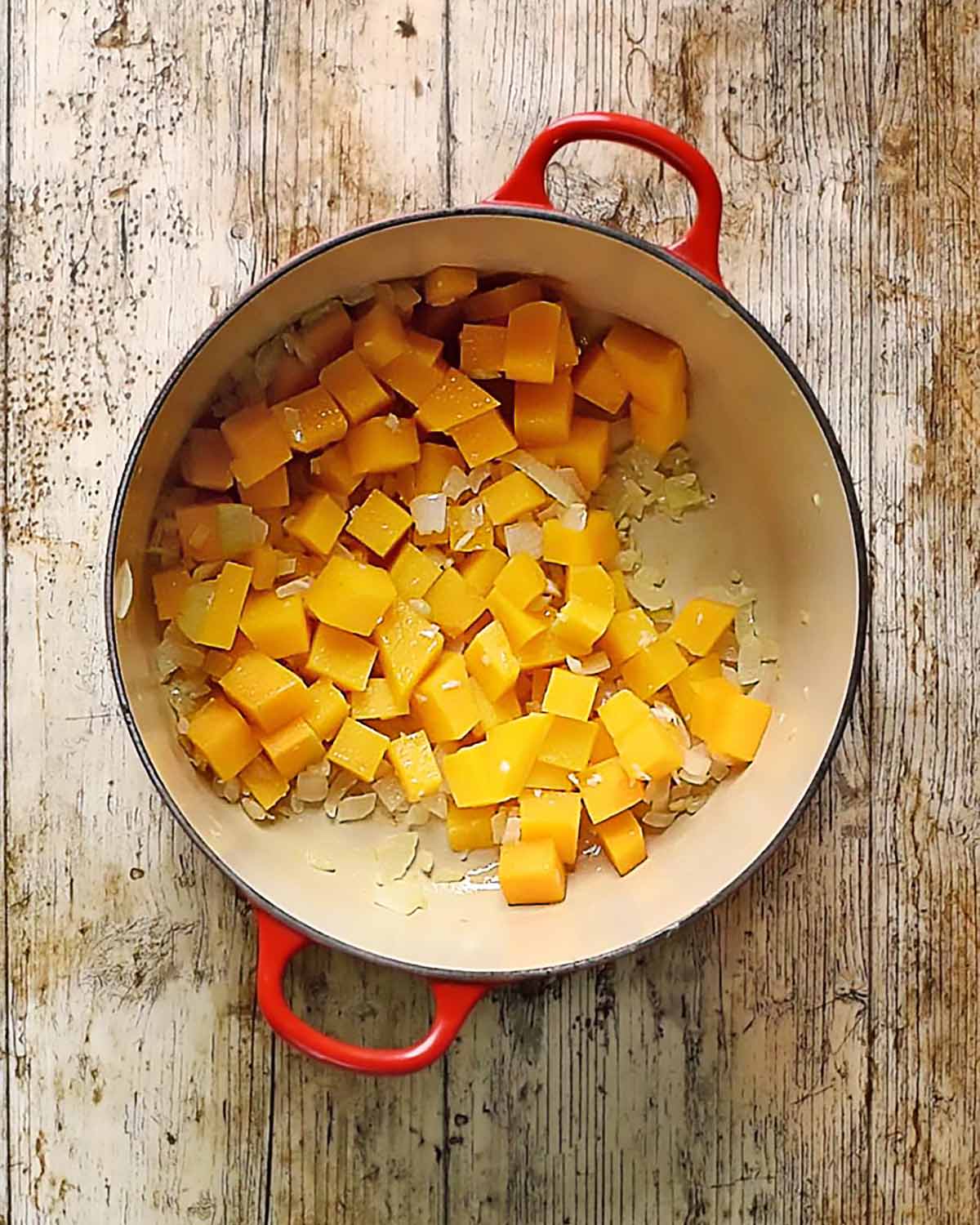 A large cooking pot with cubes of pumpkin and chopped onion cooking in it.
