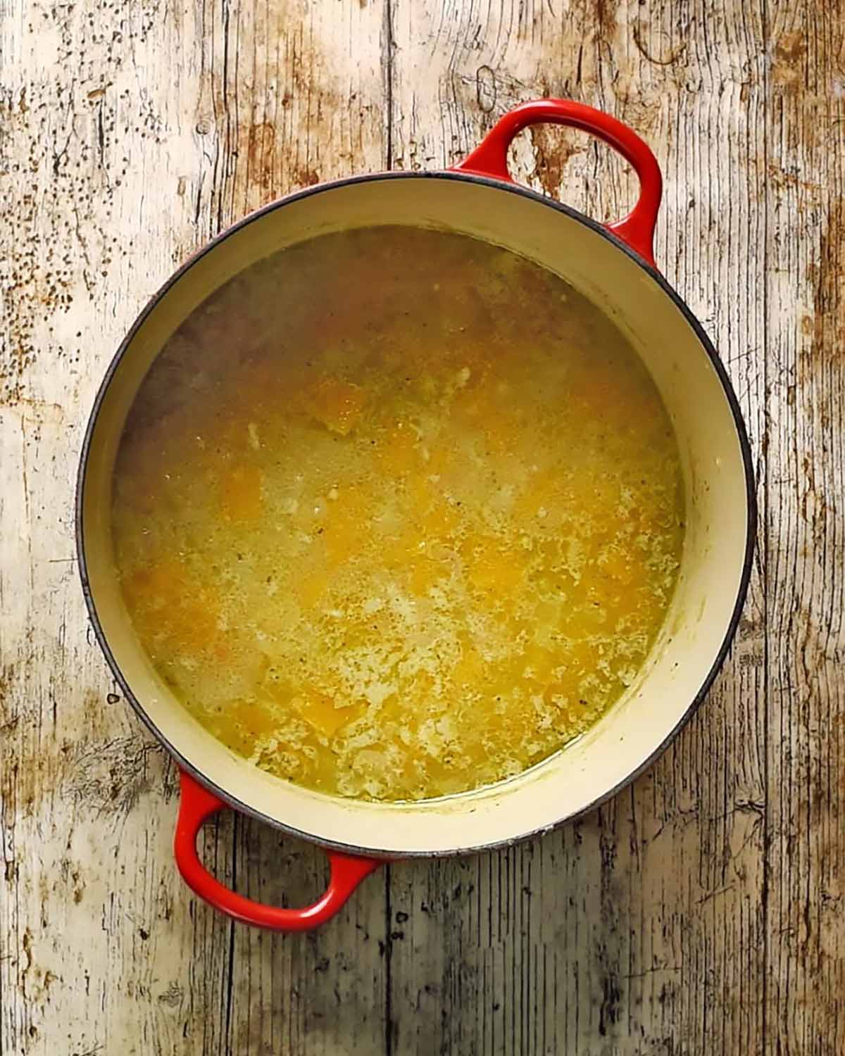 Chopped pumpkin and onion cooking in stock in a large pot.