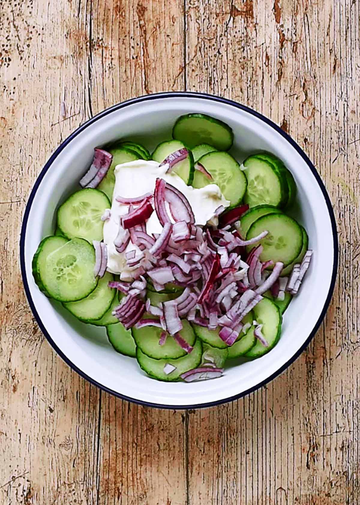 A bowl of cucumber slices with chopped red onion and a dollop of sour cream.